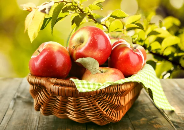 Wicker basket of red apples with napkin on nature background — Stok fotoğraf