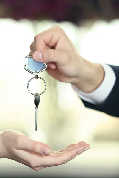 Hand av affärsmannen ger nycklar till kvinnlig hand på suddig bakgrund — Stockfoto