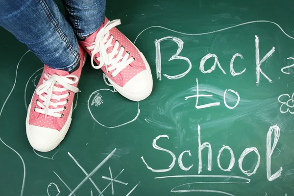 Female feet on blackboard background with inscriptions and sketches — Stock Photo, Image