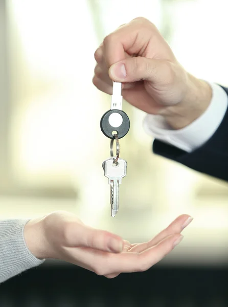 Hand eines Geschäftsmannes übergibt Schlüssel an weibliche Hand auf verschwommenem Hintergrund — Stockfoto