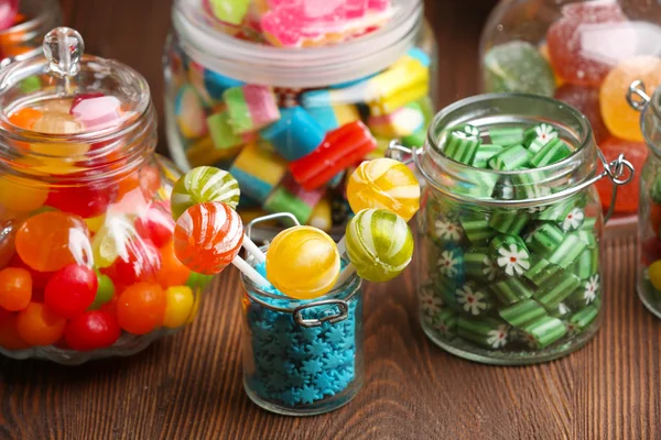Kleurrijke snoepjes in potten op tafel op houten achtergrond — Stockfoto