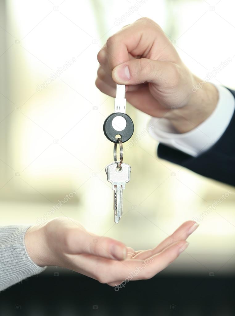 Hand of businessman giving keys to female hand on blurred background