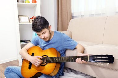 Gitarlı genç adam odada yerde yatıyor.