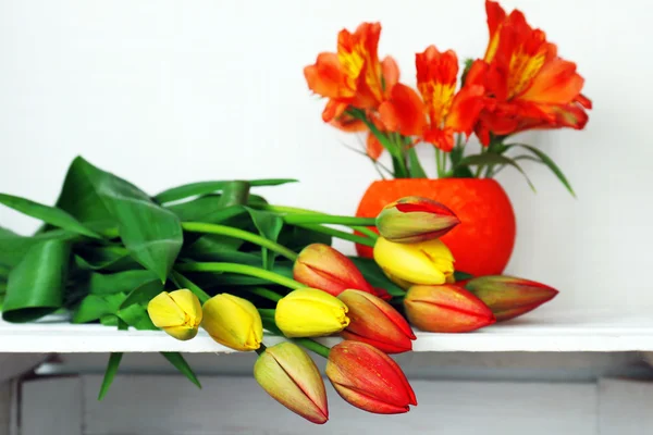 Beautiful flowers on shelf on wall background — Stock Photo, Image