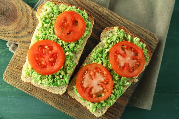 Vegansk smörgås med avokado och grönsaker på skärbräda, på trä bakgrund — Stockfoto