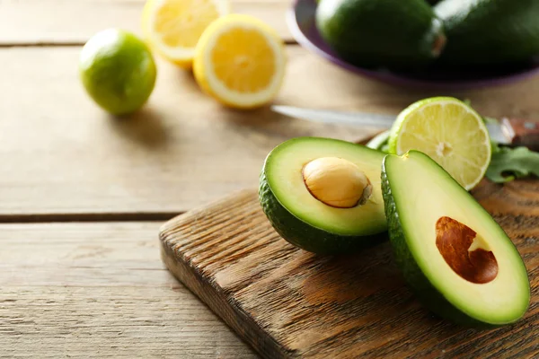 Avocado en citroen lime gesneden op snijplank, op houten achtergrond — Stockfoto