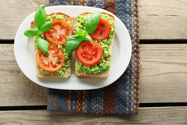 Vegan sandwich with avocado and vegetables on plate, on wooden background