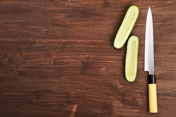 Halves of cucumber with knife on wooden background — Stock Photo, Image