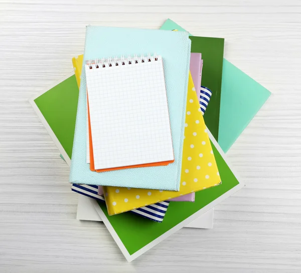 Notebook on top of pile of books and magazines on wooden background — Stock Photo, Image