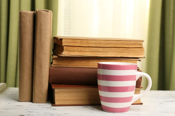 Livros e xícara sobre mesa de madeira, sobre cortinas de fundo — Fotografia de Stock