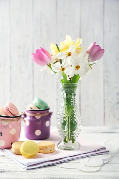 Buquê de primavera em vaso e saborosos macaroons na cor de fundo de madeira — Fotografia de Stock