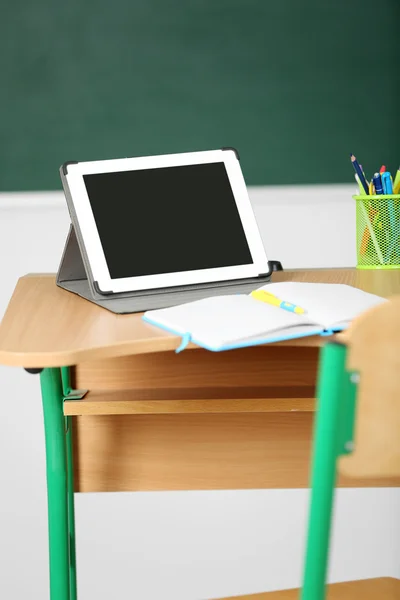 Wooden desk with stationery and tablet in class on blackboard background — Stock Photo, Image