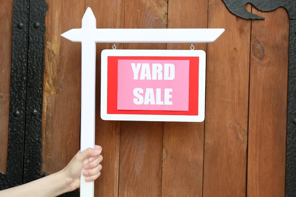 Wooden Yard Sale sign in female hand on wooden fence background — Stock Photo, Image