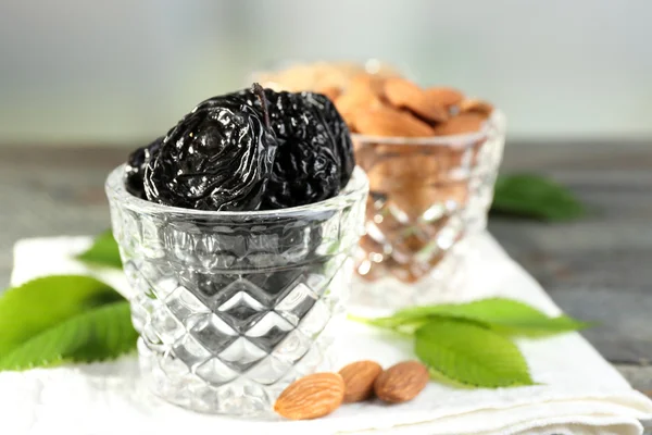 Prunes and almonds in glasses with leaves on wooden table, closeup — Stock Photo, Image