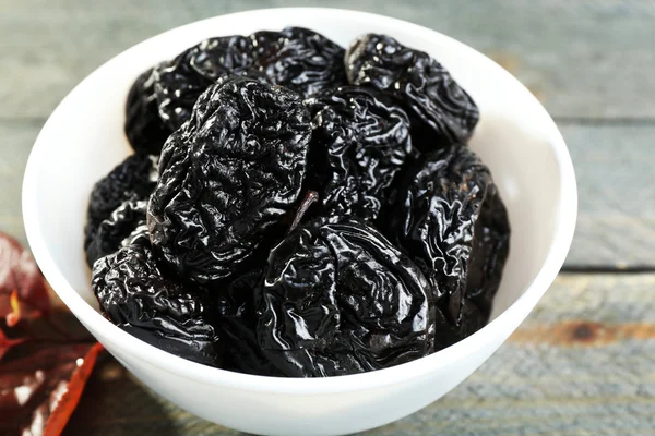 Saucer of prunes with leaves on wooden table, closeup — Stock Photo, Image