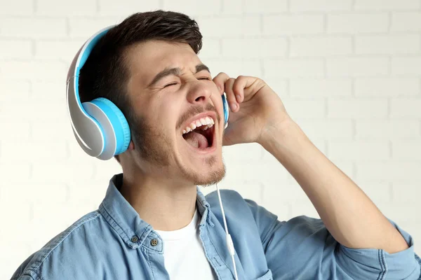 Bello giovane uomo ascoltare musica su sfondo muro di mattoni — Foto Stock