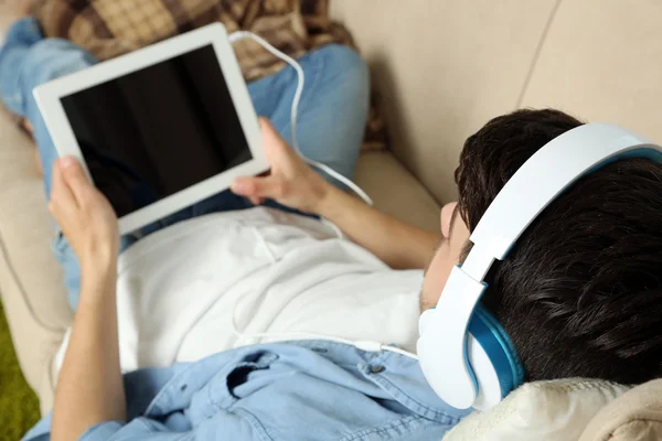 Bonito jovem deitado no sofá e ouvindo música no quarto — Fotografia de Stock