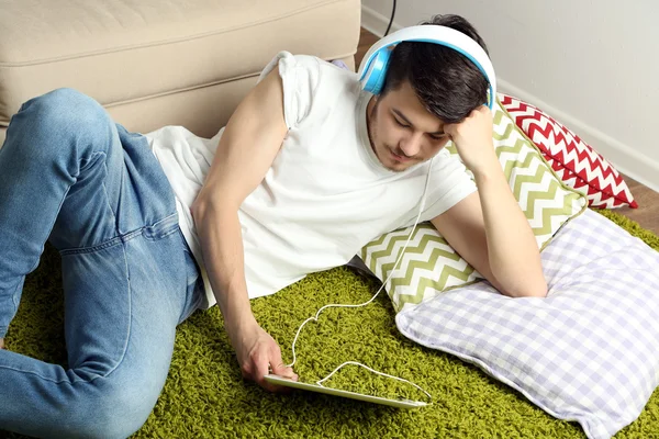 Handsome young man lying on carpet and listening to music in room — Stock Photo, Image