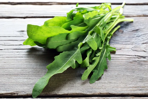 Grüne Rucolablätter auf Holztisch — Stockfoto