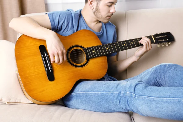 Jovem com guitarra no sofá no quarto — Fotografia de Stock