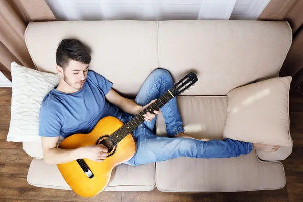 Jovem com guitarra no sofá no quarto — Fotografia de Stock