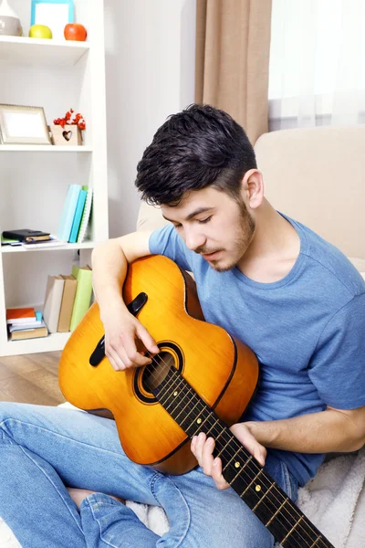 Młody człowiek z gitarą na podłodze w pokoju — Zdjęcie stockowe