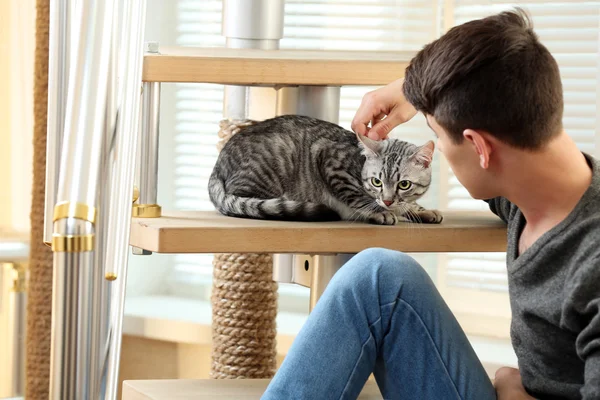 Jovem bonito com gato bonito sentado em passos em casa — Fotografia de Stock