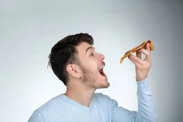 Junger Mann isst Stück Pizza auf grauem Hintergrund Stockfoto