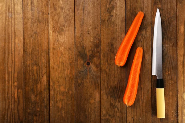 Moitiés de carotte avec couteau sur fond en bois — Photo