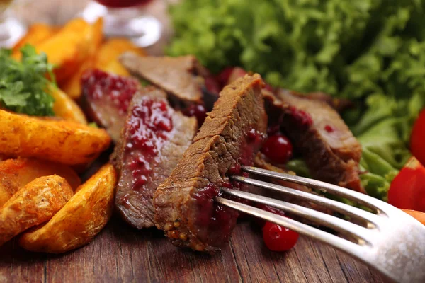 Beef with cranberry sauce, roasted potato slices and bun on cutting board, on wooden background — Stock Photo, Image