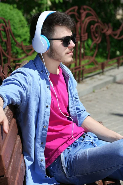 Homme avec écouteurs reposant sur le banc dans le parc — Photo