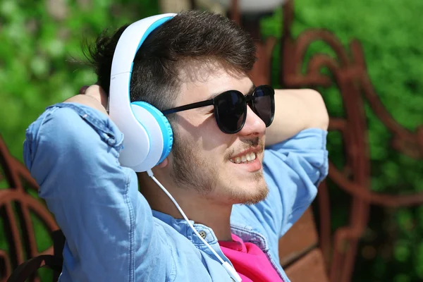 Homem com fones de ouvido descansando no banco no parque — Fotografia de Stock