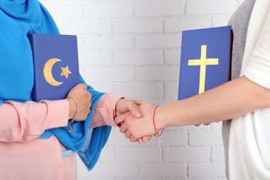 Two friends holding books with religions symbols