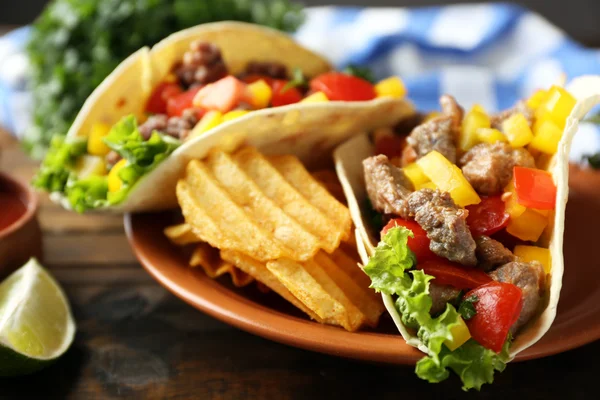 Буррито из говядины с овощами, картофельные чипсы на тарелке, на деревянном фоне — стоковое фото