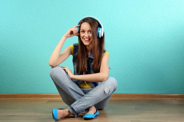 Young woman sitting on floor with headphones on turquoise wallpaper background — Stock Photo, Image