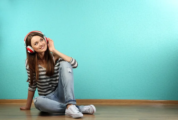 Jeune femme assise sur le sol avec écouteurs sur fond de papier peint turquoise — Photo