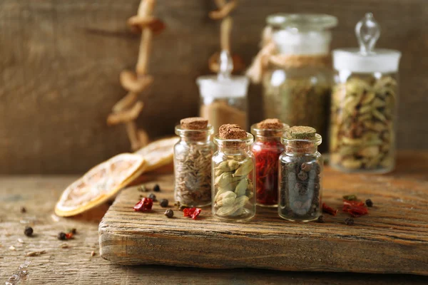 Assortiment van specerijen in glazen flessen op snijplank, op houten achtergrond — Stockfoto