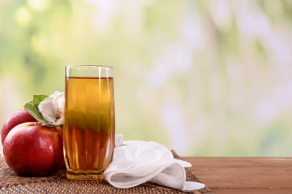 Glass of apple juice and apples on wooden table, on nature background — Stock Photo, Image