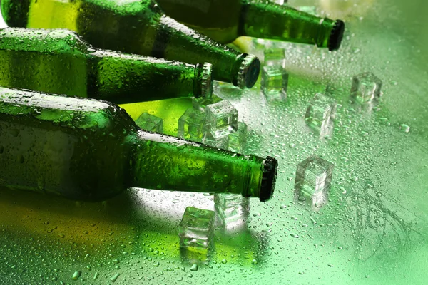 Glazen flessen bier met ijsblokjes op natte tabelachtergrond — Stockfoto