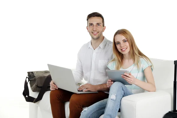 Portret młodego szczęśliwa para z bagażu, cyfrowe tabletki i laptopa siedząc na kanapie. Na białym tle — Zdjęcie stockowe