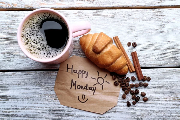 Cup of coffee with fresh croissant and Happy Monday massage on wooden table, top view