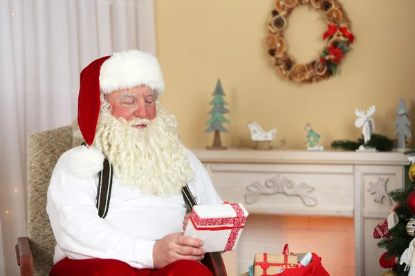 Santa Claus sitting with children presents in comfortable chair near fireplace at home — Stock Photo, Image