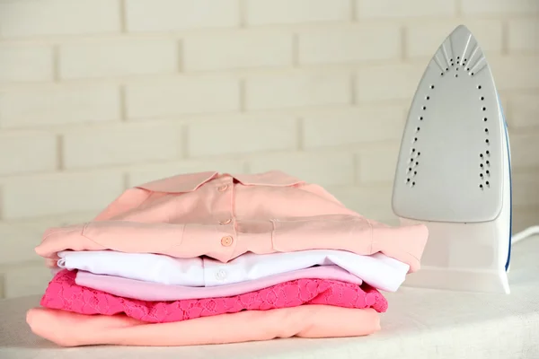 Pile of clothes and electric iron on brick wall background — Stock Photo, Image