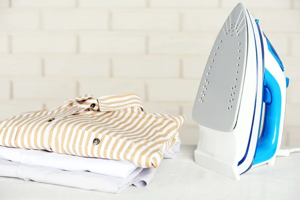 Pile of clothes and electric iron on brick wall background — Stock Photo, Image