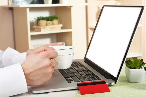 Mann hält Kreditkarte in der Hand und arbeitet am Laptop im häuslichen Innenraum — Stockfoto