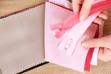 Renkli kumaş örnekleri ve ahşap masa arka plan üzerinde eller içinde fermuar