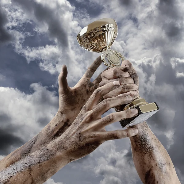 Gold cup in dirty hands on sky background — Stock Photo, Image