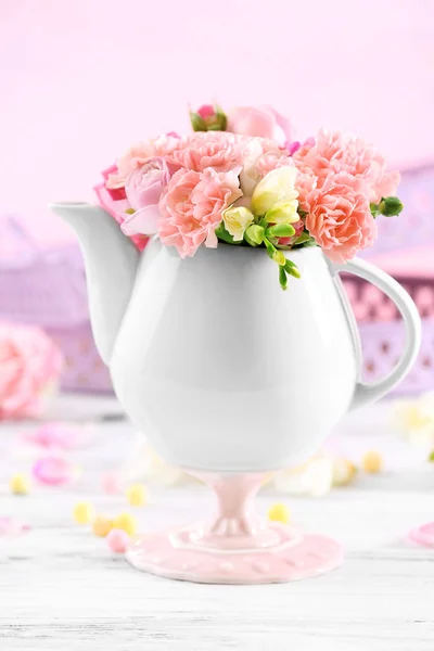 Composition with beautiful spring flowers in teapot on light pink background — Stock Photo, Image