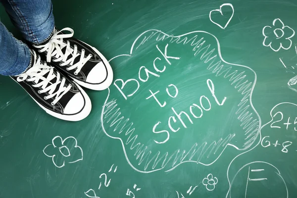 Female feet on blackboard background with inscriptions and sketches — Stock Photo, Image