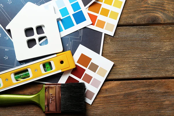 Échantillons de couleur, maison décorative, gants et pinceaux sur fond de table en bois — Photo